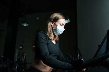 Fototapeta na wymiar Caucasian Sportswoman training on treadmill in gym and wearing face mask to protect herself against coronavirus during global pandemic of covid-19 virus