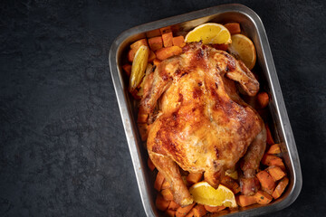 Whole baked chicken with carrots and oranges on a wooden table. Close-up and top view