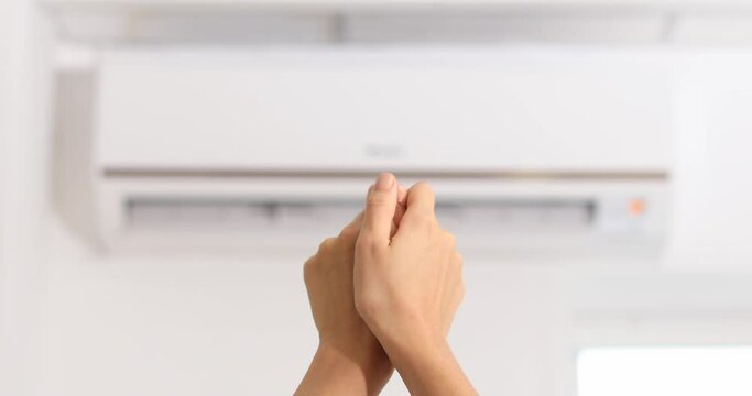 Woman warming hands under air conditioner which is operating in heating mode