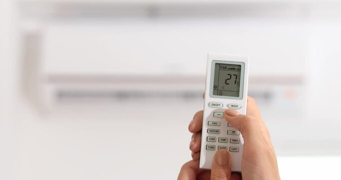 Woman adjusting temperature of air conditioner which is operating in heating mode, closeup
