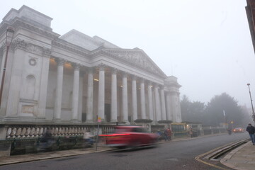 Cambridge UK December 2020 Large white building of the Fitzwilliam Museum, cars and cyclists blurred by long exposure passing by on a foggy cold december day