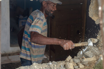 older Haitian Latino man working on construction hammering the wall to knock it down