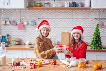 Little girls making Christmas gingerbread house at fireplace in decorated living room.