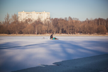 A lone fisherman sits on a frozen pond covered with snow.
