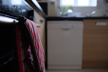 Close wide shot of red oven mittens hanging on the handle of the oven, dark kitchen in a modern...