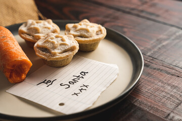 Carrot and yummy mince pies on a dish with a note "To Santa", a Christmas treat for Santa Claus © Max Rushent/Wirestock