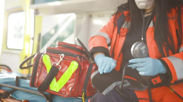 Female paramedic packs sphygmomanometer sitting inside an emergency vehicle