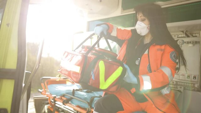 Experienced female paramedic in face mask checks equipment bag