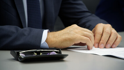 Hands of an official or businessman sitting at the table - a participant in a press conference, meeting or negotiations. Glasses and documents.
