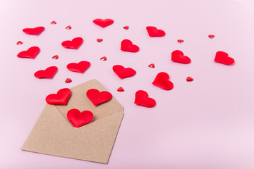 Red hearts fly out of craft paper envelope on light pink background. Valentine day. love concept. Gift, message for lover. Space for text.