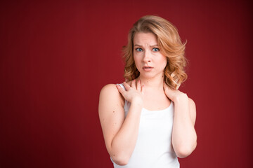 Blond woman in white tank top looks terrified or shocked on red background.