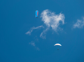 Two paragliders fly over a blue sky. Kiting in blue and orange kite in Stubai valley Tirol Alps, Austria, Summer