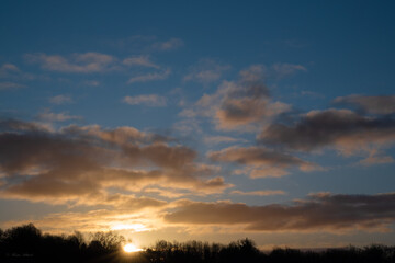 Fototapeta na wymiar sunrise peeping above the treeline, blue sky and illuminated clouds