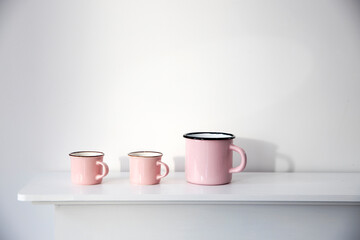 Fototapeta na wymiar Three small pink pastel coffee cups on a white console against a wall background.