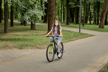 Naklejka premium A beautiful girl with long hair rides a Bicycle in the Park in the summer on a tiled path. Outdoor activity.