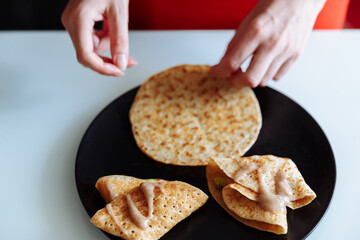 Woman's hand decorates pancakes with a fruits kiwi and banana. Black plate, white table