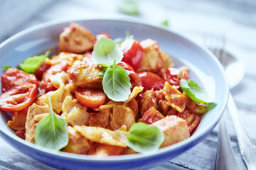 Farfalle pasta with chicken breast, cherry tomatoes and fresh basil. Bright wooden background. Close up.