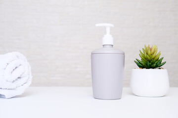 Gray soap dispenser, white towel and potted plant for spa, body and face care, bathroom interior in pastel colors with copy space