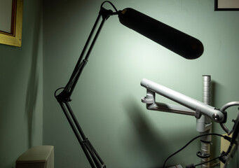 Articulated desk lamp with black arms in foreground blur and articulated monitor stand.