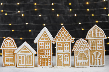 Gingerbread houses on the background of garland lights. New Year's traditional treats. Glazed Christmas cookies.
