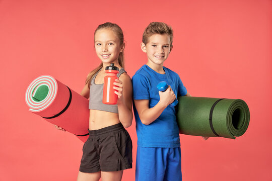 Joyful kids with sports equipment standing against red background