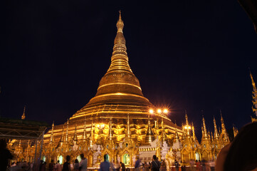 a large building with a tall pointy tower at night with Shwedagon Pagoda in the background