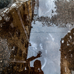 Silhouette of man reflected in dirty puddle