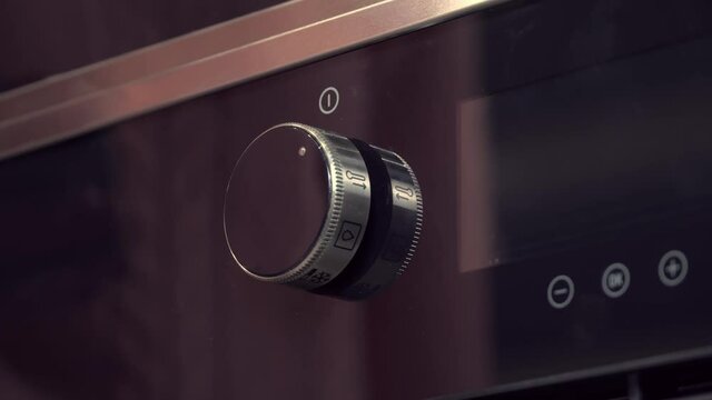 Manual activation of the temperature switch of the black electric stove oven in the home kitchen