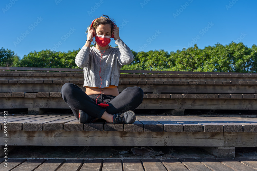 Sticker Shot of a sitting woman in a protective mask with headphones talking by phone - new normal