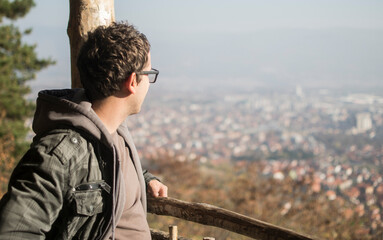 Young man on forest view point looking at the city