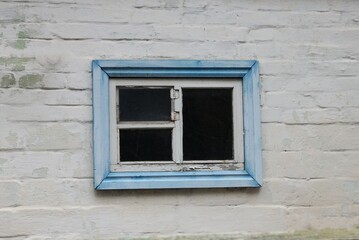small old window in a blue wooden frame on a white brick wall of a rural house