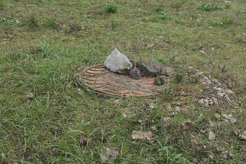 one brown rusty iron manhole with gray stones in green grass outside