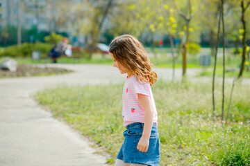 beautiful little girl with developing hair walks in street violating quarantine of coronavirus. girl in pink T-shirt runs across green field. girl plays active games in nature in summer or spring.