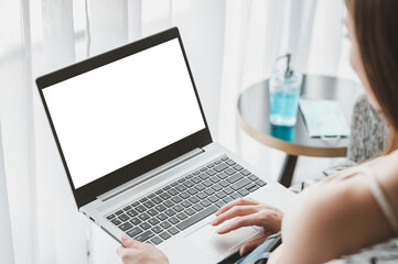 back view of woman using laptop computer with blank copy space screen with surgical face mask and alcohol gel in background by window