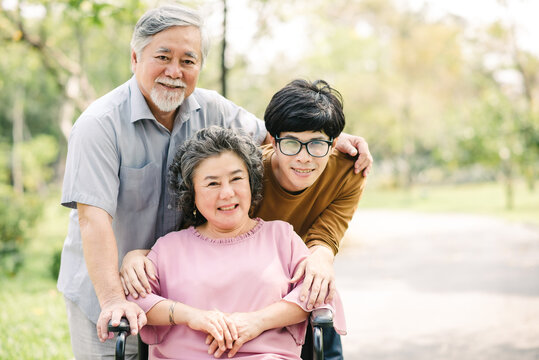 Happy Asian family with young man and senior man and woman in wheelchair embeacing each other in the park