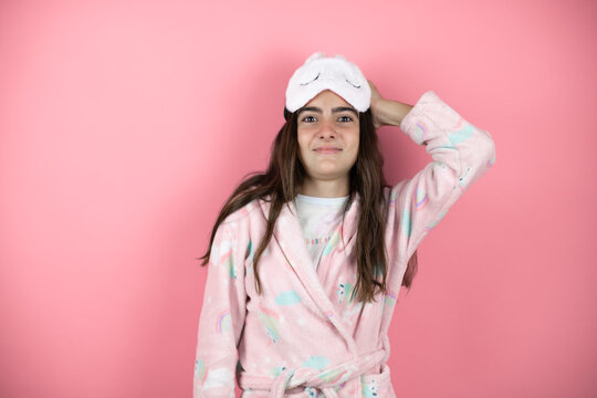 Pretty Girl Wearing Pajamas And Sleep Mask Over Pink Background Putting One Hand On Her Head Smiling Like She Had Forgotten Something