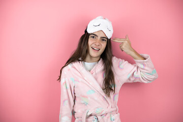 Pretty girl wearing pajamas and sleep mask over pink background Shooting and killing oneself pointing hand and fingers to head like gun, suicide gesture.