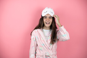 Pretty girl wearing pajamas and sleep mask over pink background confused and wondering about question. Uncertain with doubt, thinking with hand on head