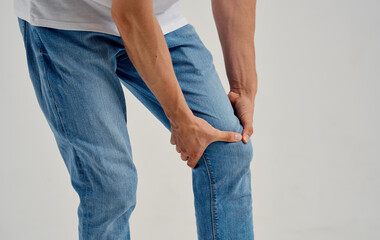 man in jeans touches his knee with his hands on a light background cropped view