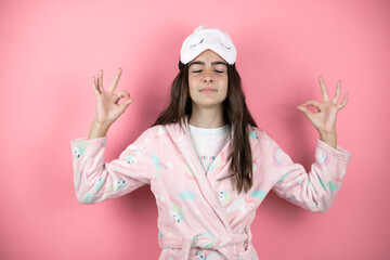 Pretty girl wearing pajamas and sleep mask over pink background relax and smiling with eyes closed doing meditation gesture with fingers