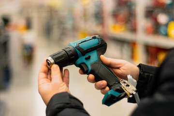Naklejka premium Man holds in his hands a green cordless screwdriver for repair work on the background of showcases in a hardware store.