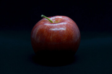 Red apple in light and shadows on black background