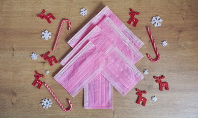 Christmas tree made of pink surgical masks with colorful red and white Christmas ornaments and decorations on a warm wooden background. Safe Christmas or medical background. 