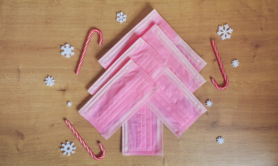 Christmas tree made of pink surgical masks with colorful Christmas ornaments and decorations on a warm wooden background. Safe Christmas or medical background. 