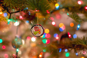 Sushi roll Christmas ornament hanging on a pine tree decorated with colorful lights with a blurry bokeh background