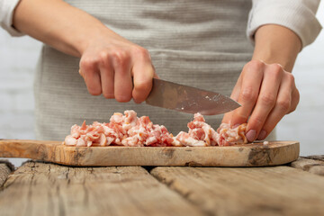 Macro shot of professional chef cuts with knife bacon on wooden chopped board for cooking pasta alla carbonara. Preparing traditional italian dish on white background. Cooking process concept.