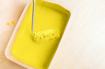 roller collects Illuminating yellow paint before painting from a transparent form on the plywood...