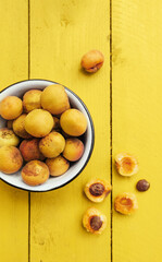 ripe juicy homemade apricots with cracks and flaws in the plate and scattered on a bright yellow wooden surface. tinting Illuminating color of year 2021