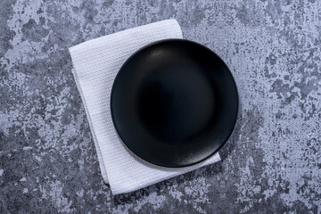 Black plate, cutlery and napkin on rustic stone table top view. Table setting.