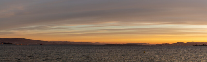 banner panorama of sunset over a calm ocean with hills and mountains in the background